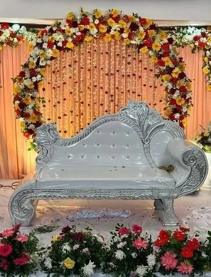 A traditional reception stage featuring a silver-carved sofa. The backdrop is a mix of drapes and a floral arch, creating a classic and regal look.
