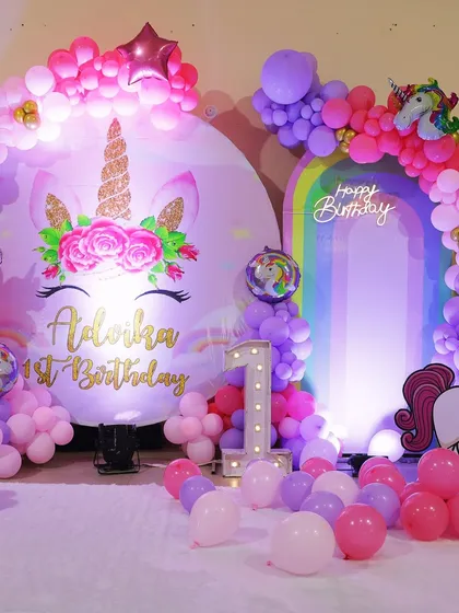 A magical unicorn theme perfect for a first birthday. This setup features a large unicorn backdrop, a rainbow arch, and a light-up number '1' to celebrate the big milestone.