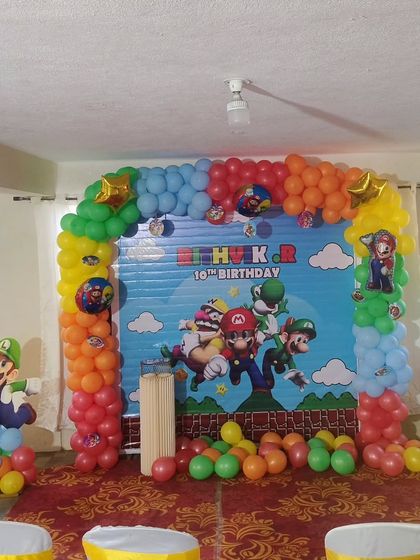A Super Mario Bros themed party with a large backdrop featuring all the characters and a colorful balloon arch.