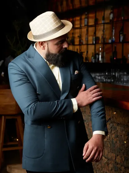 A clean cut and a confident fit. This image captures a client wearing the deep teal suit in a relaxed, stylish setting, defining modern sophistication.