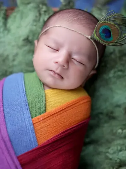 A close-up of a baby girl in our Krishna-inspired setup, with a peacock feather headband and a colorful wrap. We adapt our themes for both baby boys and girls.