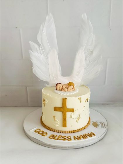 A serene and beautiful baptism cake with a golden cross, delicate angel wings, and a sleeping baby topper.