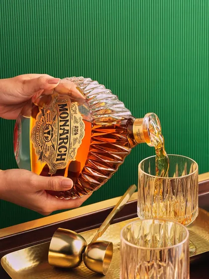 A lifestyle pour shot for Monarch brandy. The hands holding the bottle add a human element, making the scene feel warm and inviting. The rich green background complements the amber liquid beautifully.