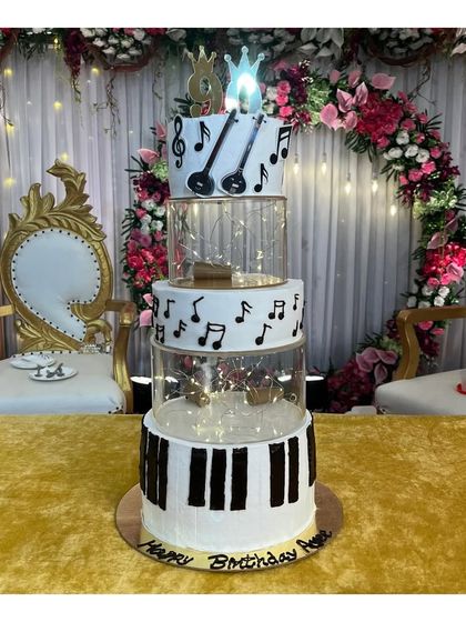 A magnificent 5-tier spacer cake with a music theme for a 60th birthday. This blueberry-flavored cake features piano keys, musical notes, and a guitar topper, all brought together with fairy lights in the spacers.