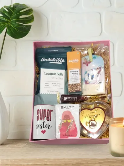 A perfect Rakhi hamper for your 'Super Sister'. This set includes a special mug, healthy snacks like coconut balls and cranberry almond bars, chocolates, and a scented candle.