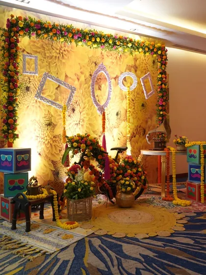 A fun and quirky photo booth for a Haldi ceremony. The backdrop of yellow flowers is accented with empty vintage frames, a flower-adorned bicycle, and playful props.