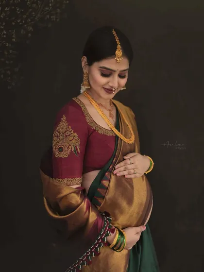 A close-up focusing on the tender connection between mother and baby. Her gentle touch on the bump, combined with the rich textures of the silk saree, makes for a deeply emotional and artistic portrait.