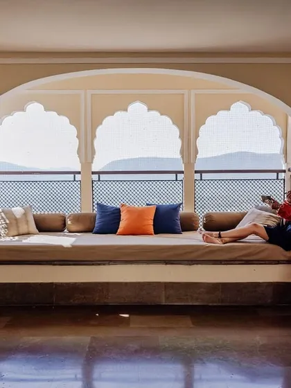 A moment of quiet contemplation for the bride before her wedding at Alila Fort. Her red lehenga is laid out, and she looks out at the Aravalli hills from a traditional jharokha window.