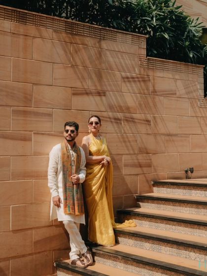 A stylish, editorial-style portrait of the couple on a staircase during their Haldi event, showcasing their coordinated yellow outfits.