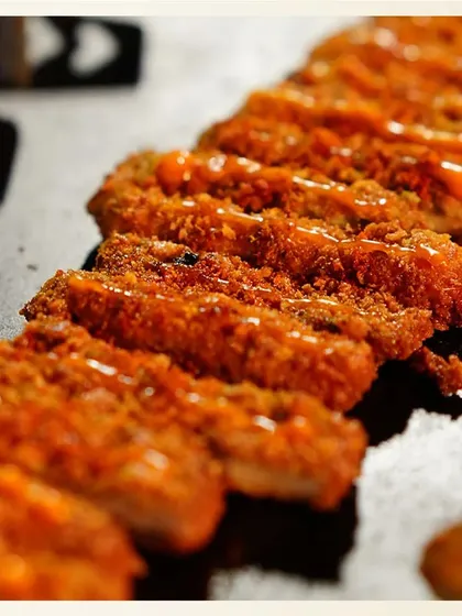 A platter of our Dukkah Spice Cottage Cheese, sliced and arranged for serving. The close-up shot details the crunchy coating and the drizzle of sauce on top.