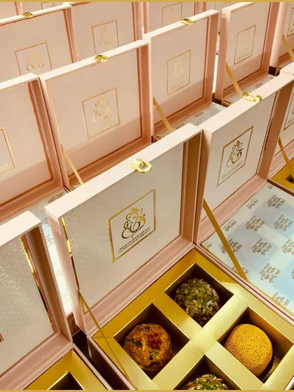 We specialize in personalized wedding gifts. These elegant pink and gold boxes feature a custom monogram for the couple, filled with delicious laddus for a sweet beginning.