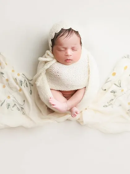 A simple, artistic shot. The baby is wrapped in white, with a beautiful floral fabric flowing out like wings, creating a truly angelic look.