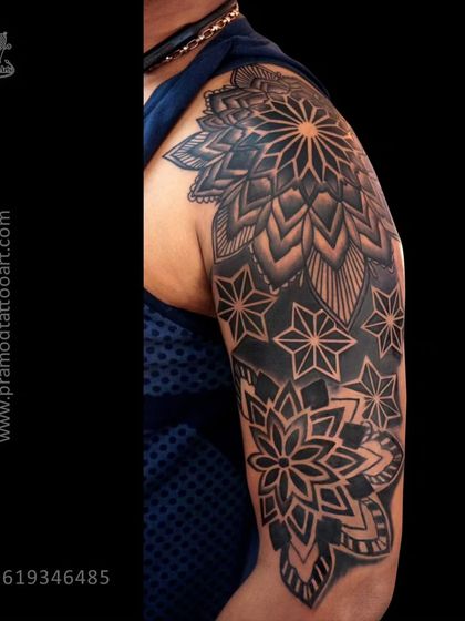 A large shoulder and bicep tattoo with intricate mandala and geometric patterns. The heavy blackwork makes this a very bold and impactful piece.