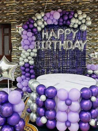 A purple and silver balloon decoration with a fringe backdrop and a balloon-covered cake table.