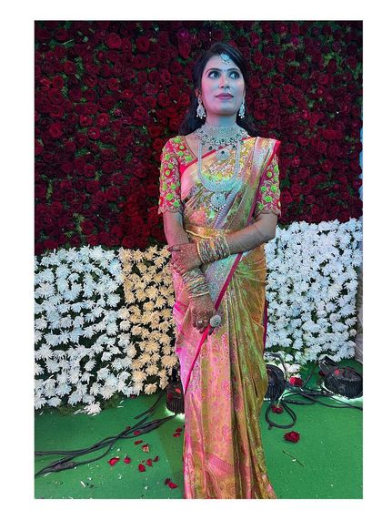 The bride posing against a beautiful floral backdrop. Her gold silk saree and diamond jewellery are complemented by a radiant and glamorous makeup look.
