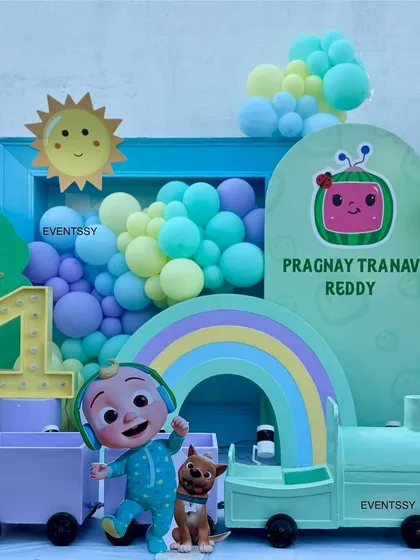 This Cocomelon theme features a light-up number '1', a pastel train, and a smiling sun prop for a cheerful first birthday.
