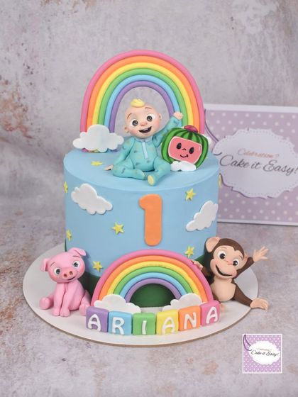 A Cocomelon cake is always a hit for a first birthday. This one features JJ, a rainbow, and his animal friends, including a pig and a monkey, creating a colorful and cheerful scene.