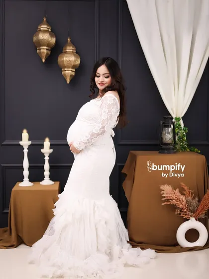 A beautiful solo portrait of a mom-to-be in a white lace mermaid gown. The dark, moody backdrop with Moroccan-style lanterns creates a sophisticated and elegant atmosphere.