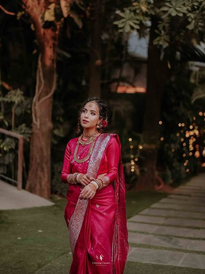 The bride in her pink wedding saree, looking ethereal as she walks through a garden at dusk.