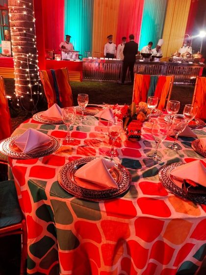 A beautifully set dining table at a colorful outdoor event. The vibrant tablecloth, silver charger plates, and elegant glassware show my attention to detail in every aspect of event catering.