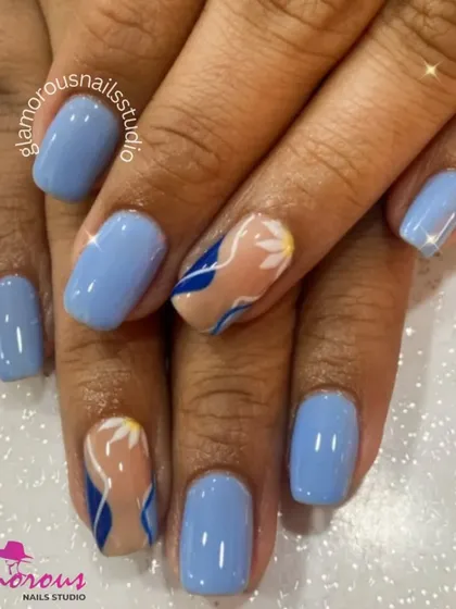 A chic and simple design with solid light blue nails and accent nails featuring an abstract pattern in shades of blue on a nude base.