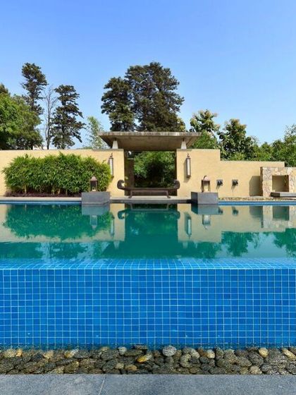 A view across the infinity edge of the C Farm pool. The design uses a dark tile to create a deep, reflective surface that mirrors the sky, while the stone surround and pebble-lined overflow connect the pool to the earthy material palette of the landscape.