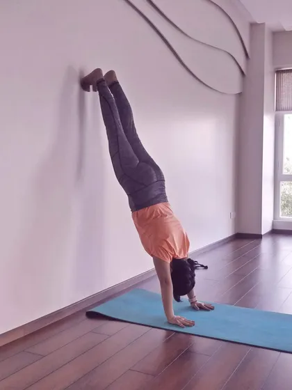 A student practices a handstand against the wall, building shoulder strength and endurance. The wall is an invaluable teacher on the path to mastering inversions.