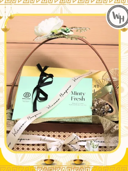 A special Diwali collaboration with Brillare, this hamper combines skincare with festive treats. The "Minty Fresh" product is the star, nestled in a wicker basket with a custom ribbon and elegant floral decoration.