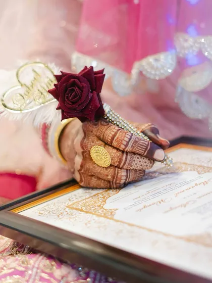 A detail shot focusing on the bride's hand, adorned with henna and holding a rose, resting on the Nikaahnama. This image is rich with symbolism and beauty.