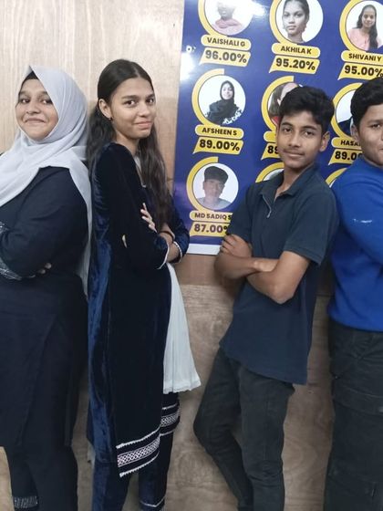 Four students strike a pose in their matching outfits, standing in front of our wall of achievers on Twinning Day.