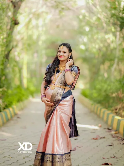 A classic solo maternity pose in a beautiful silk saree, captured on a tree-lined path.