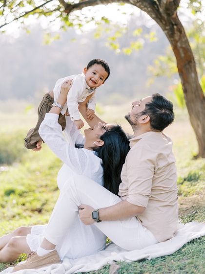 A family enjoying a picnic, with the father lifting their son high. The joy on everyone's faces is evident.