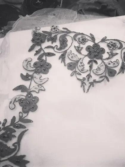 A work in progress. This black and white photo highlights the form and structure of a floral embroidery pattern being crafted on sheer fabric, showcasing the artistry before it becomes part of a finished garment.