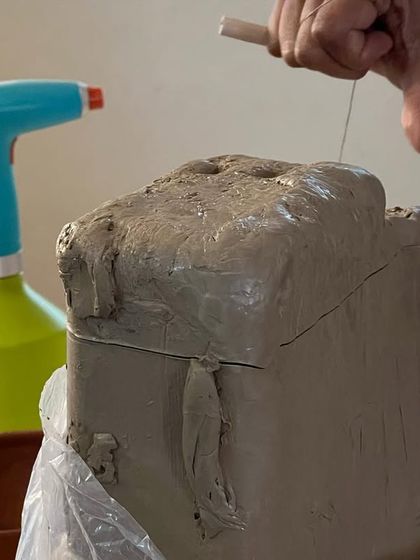 Preparing a block of clay by cutting it with a wire tool. This process, known as wedging, removes air bubbles and ensures the clay has a consistent texture, making it ready for sculpting or throwing.