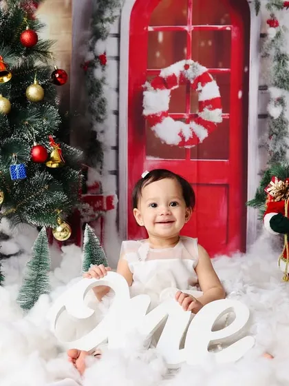 Combining two celebrations in one. This little girl marks her first birthday amidst a magical Christmas setup, complete with a tree, snowman, and a festive 'one' sign.