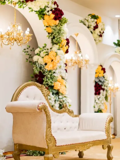 A close-up of the intricate floral work and classic seating from one of our Vashi wedding projects. The combination of a vintage-style chaise lounge with vibrant flower arrangements creates a picture-perfect setting.