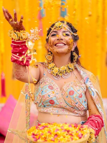 A bride joyfully tosses flower petals during her Haldi ceremony. Her face, glowing with turmeric and happiness, is the centerpiece of this vibrant and energetic shot.