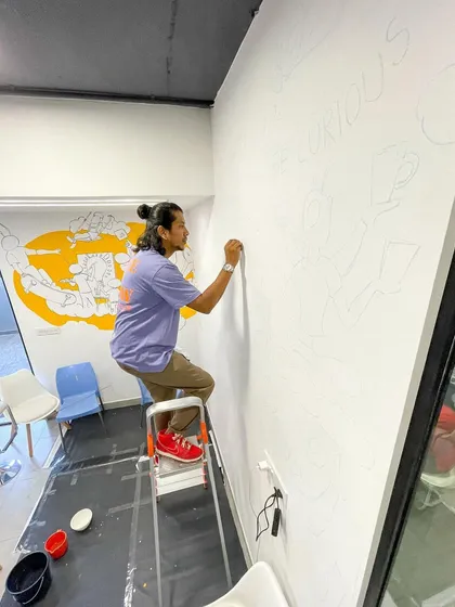 Standing on a ladder, I begin the outlining process for a large corporate mural. This foundational step is crucial for mapping out the entire composition before the details and colors are filled in.