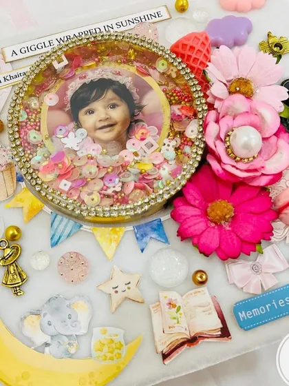 The stunning, handcrafted cover of the baby album, featuring a shaker frame, flowers, and other delicate embellishments.