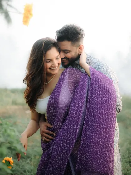 A warm, candid moment of a couple wrapped in a beautiful purple saree. The soft light and genuine smiles make this a perfect example of a relaxed and intimate outdoor couple shoot.