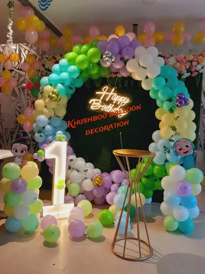 A Cocomelon first birthday party with a character-themed balloon ring, a neon sign, and a light-up marquee number '1'.