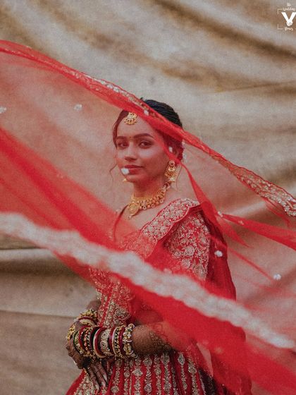 A captivating portrait of the bride, her face partially veiled by her flowing red dupatta. The movement and color create a dynamic and artistic shot.