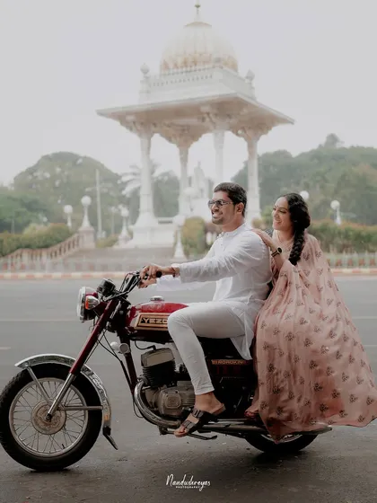 A couple enjoys a ride on a classic Yezdi motorcycle through the streets of Mysore, blending vintage charm with the city's royal heritage. This shows how we can create a unique, themed pre-wedding shoot.