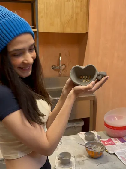 A happy participant at our workshop proudly shows off her heart-shaped mug, inscribed with the words 'SELF LOVE'. Our workshops are a space to unwind, connect with your creativity, and make something that is truly yours.