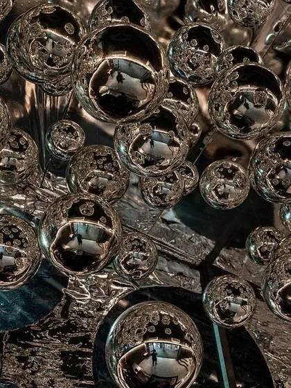 A close-up of the ceiling of the 'Silver Escapade' installation, where mirrored orbs are suspended against a reflective, textured surface. The effect is disorienting and dream-like.