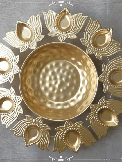A stunning golden urli platter with an outer ring of lotus-shaped diyas. This piece is a perfect centerpiece for Diwali or any pooja, designed to be filled with water, flowers, or festive treats.