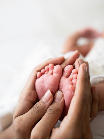 A close-up of perfectly pink newborn feet held in a parent's hands. The focus is sharp on the tiny toes, creating a beautiful macro shot.