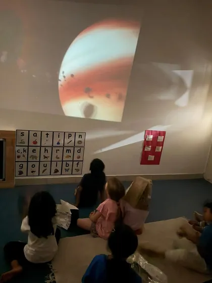 I make abstract concepts like space exploration feel magical and accessible. Here, children are captivated by a projection of planets on the wall, sparking their curiosity about the universe in a calm and immersive setting.