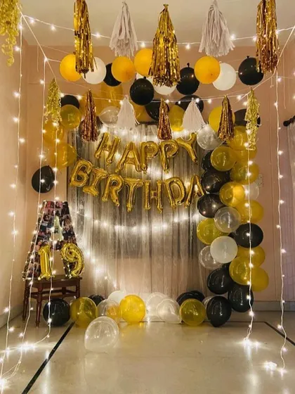 A cozy and intimate birthday setup at home. We used a curtain of fairy lights as a backdrop for the 'Happy Birthday' foil balloons, with a simple black, gold, and white balloon garland.
