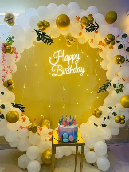 A classic white and gold balloon ring with a cake pedestal. This elegant setup is accented with fairy lights and green foliage for a touch of nature.